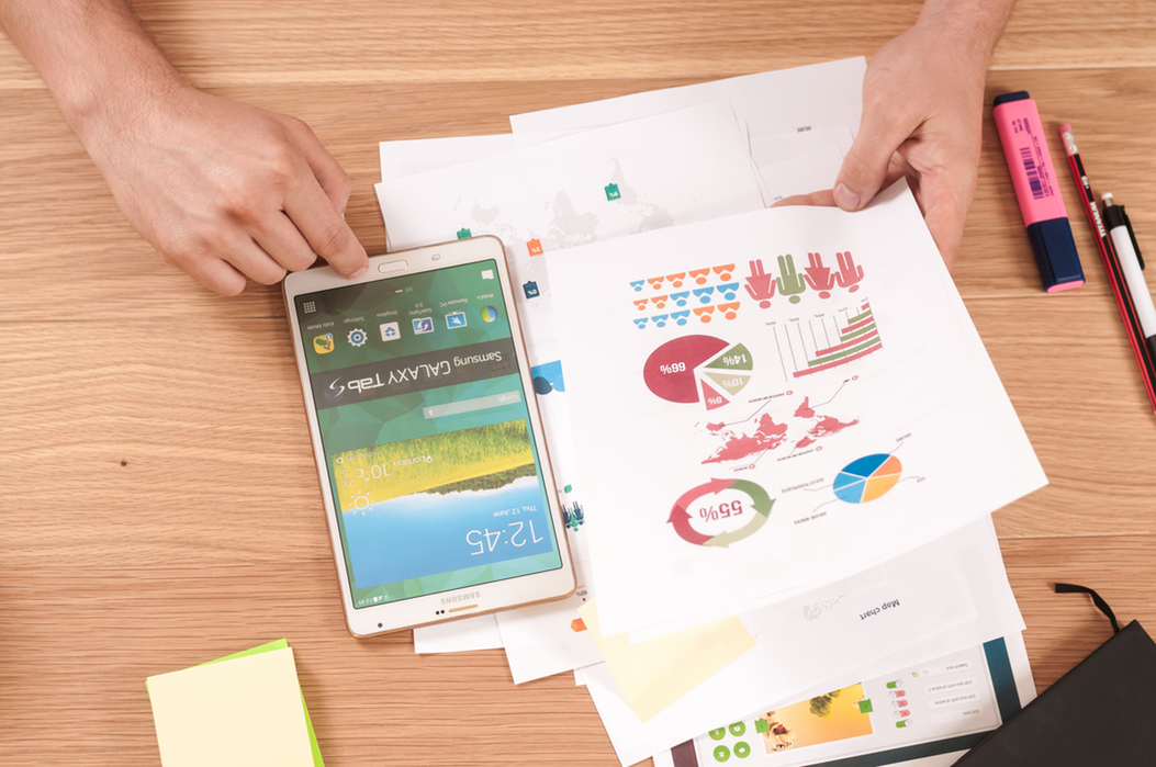 photo of a desk with someone working with paper showing graph, pie charts and a phone