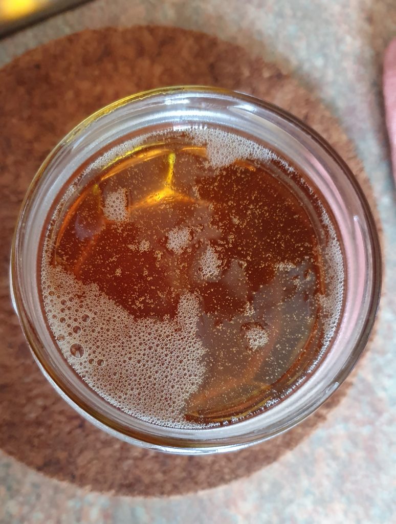 view from above the glass jar where the honey has been poured, it's honey colour with lots of little bubbles inside and at the surface