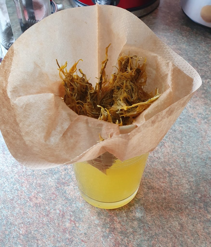 petals in a coffee filter over a glass, with yellowish liquid running through the filter