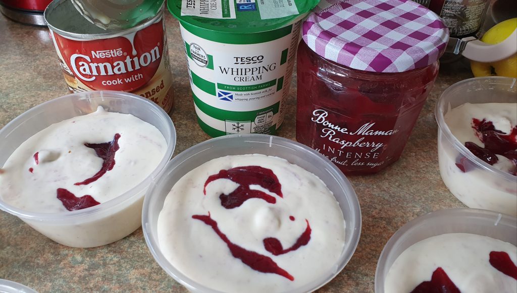 little pots of ice cream with trace of jam at the top, behind, there is a pot of whipping cream, a pot of jam and a tin of condensed milk