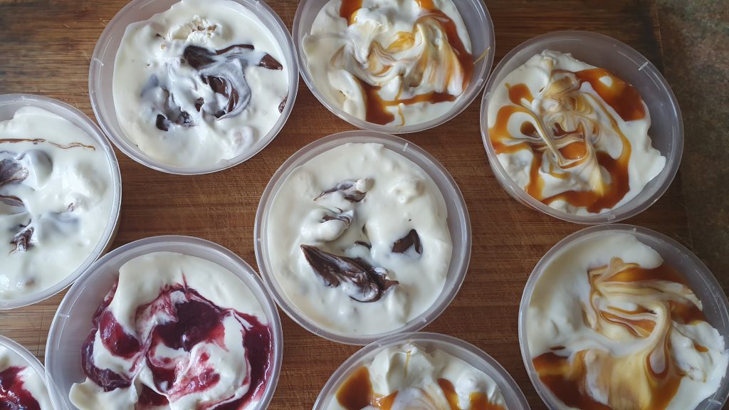 small pots of ice cream just made, some with raspberry jam at the top, others with caramel and some with chocolate