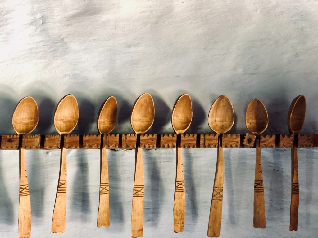 row of wooden spoons, held on a wood rail attached to a white uneven wall
