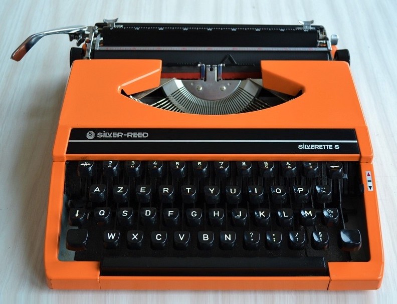 real typewriter with an orange body, black keys, the keyboard is an AZERTY as it's French