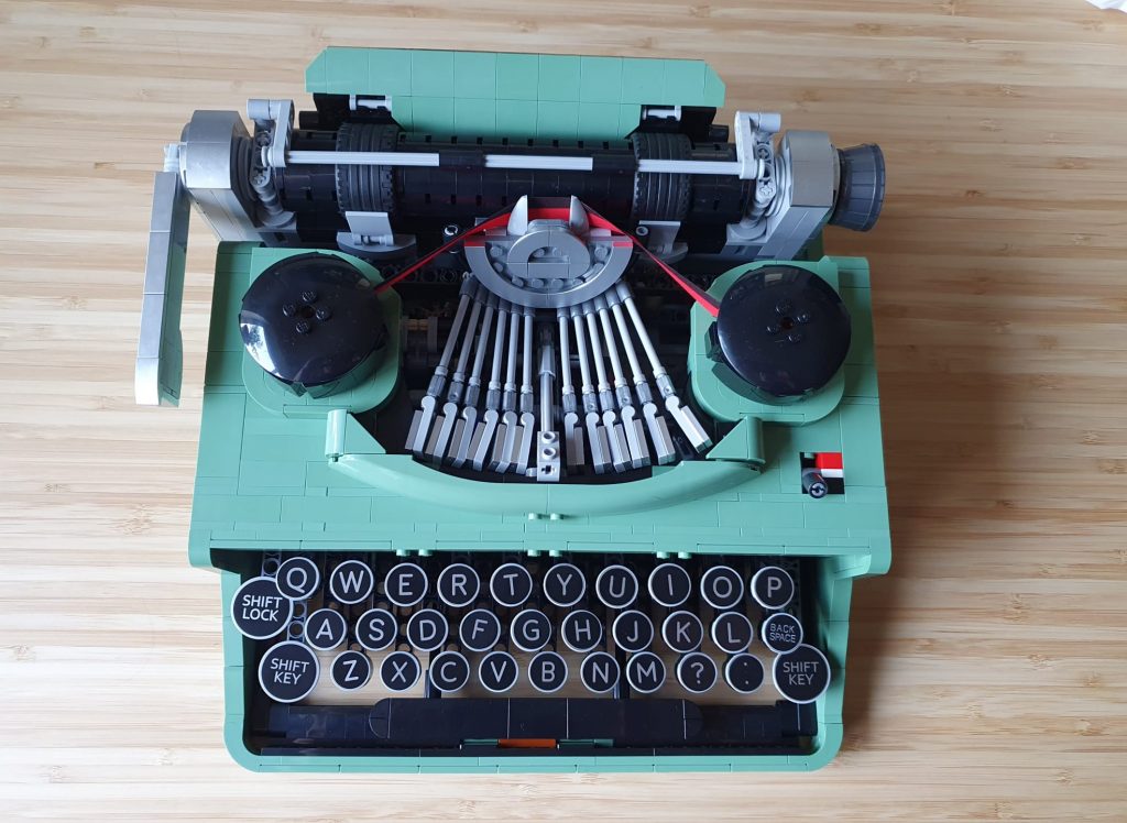 the typewrite made of lego on a wood table, it's seen from above and part of of mechanism is visible, with ink ribbon and round keys.