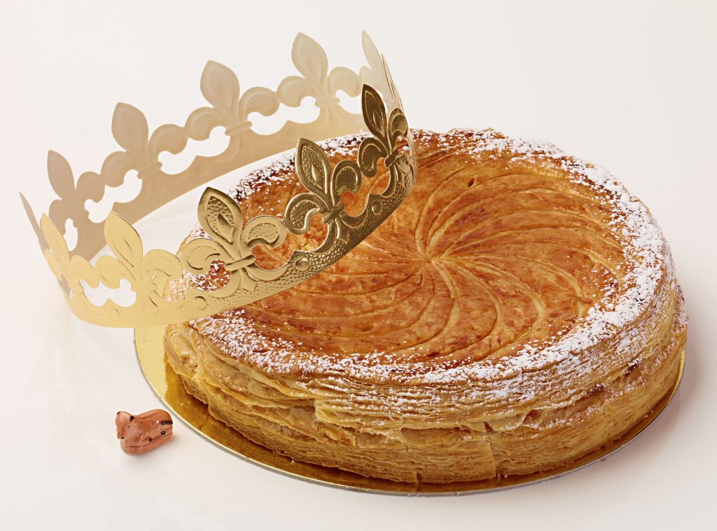 round galette with curve lines from the centre to the edge as decoration, with a golden paper crown on it and a little stone in the shape of animal on the side.