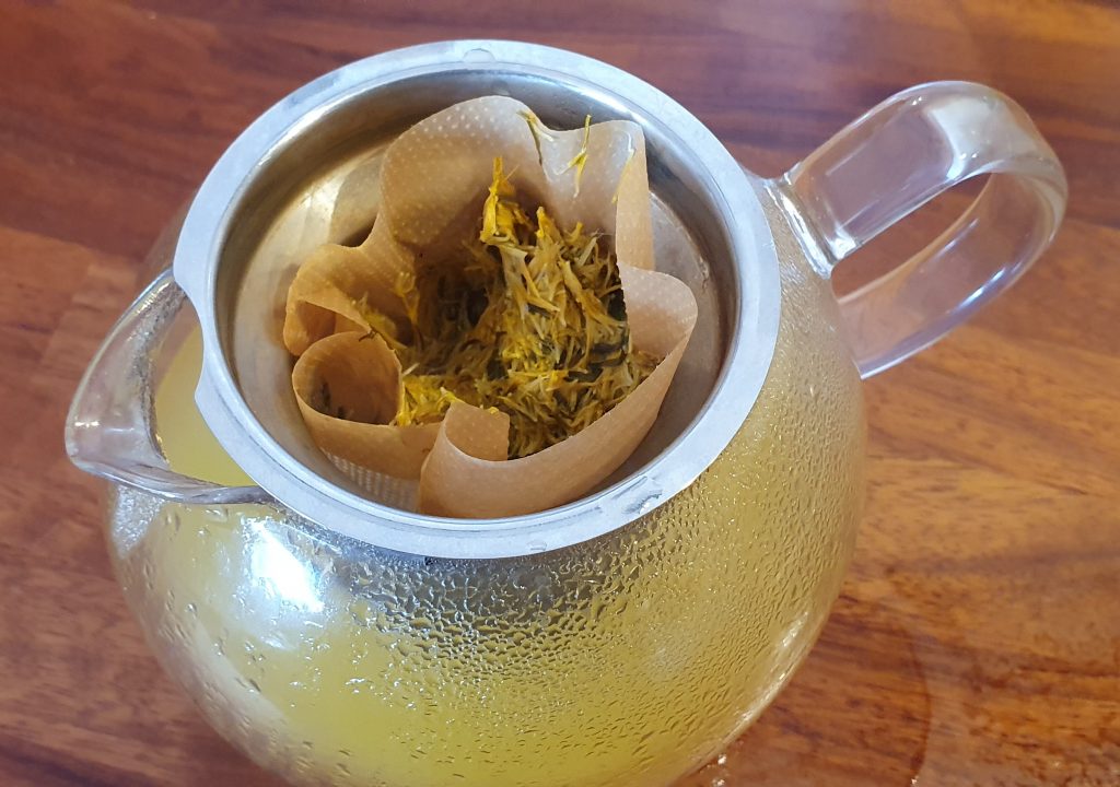 petals in a coffee filter over a teapot, with yellowish liquid running through the filter