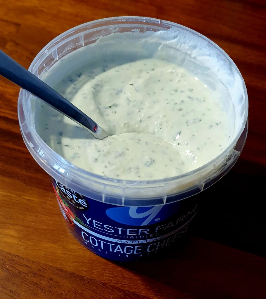 a plastic pot filled with a white dip sauce and herbes