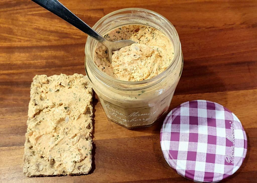 a slice of toast with some orange-y spread on it next to a pot of the same spread