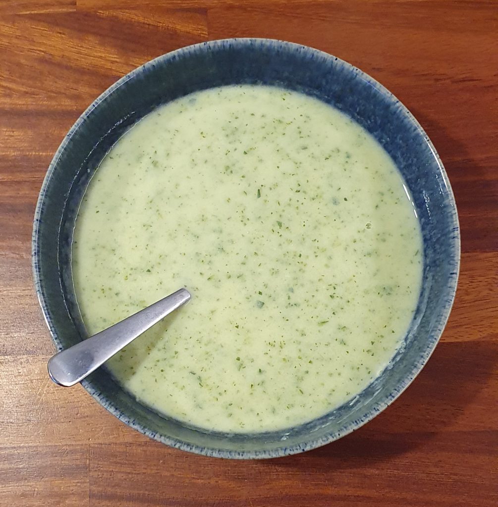 dark blue bowl with light green soupe and what looks like herbs in it