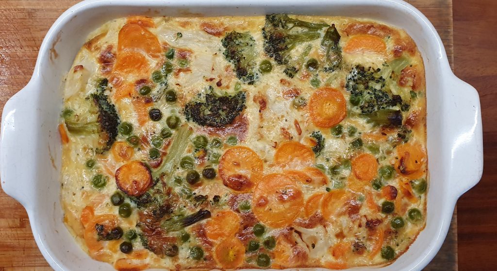 a white dish with carrots, peas and brocoli brought together with an omelet-looking-dough