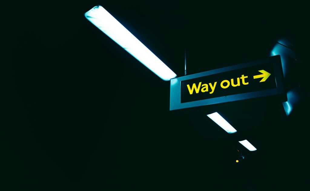 a dark space with a black and yellow sign that says way out,with a white neon light above it