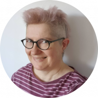 Stephanie with short pinkish hair, black round framed glasses, wearing a stripy teeshirt and smiling at the camera