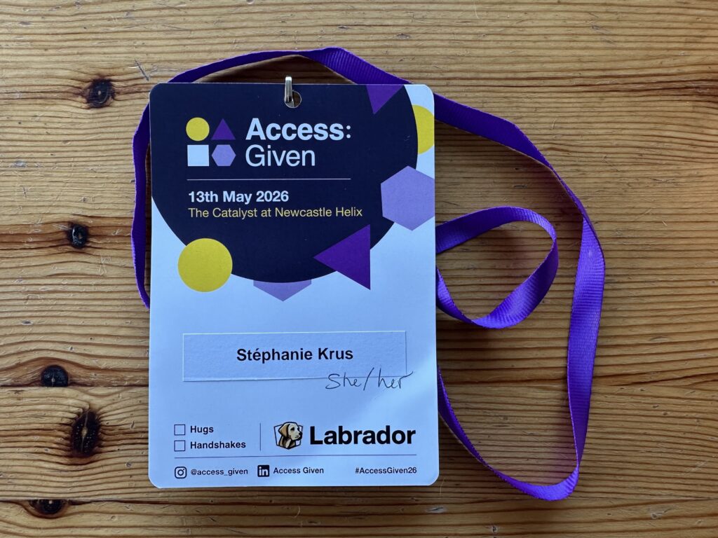 Badge for the conference with a purple lanyard. The name and date of the conference is on it and my name is printed. Underneath there are two checkboxes for Hugs and Handshakes.